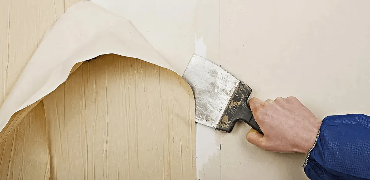 Handyman removing wallpaper with a scraper for wall preparation in Oakland, CA